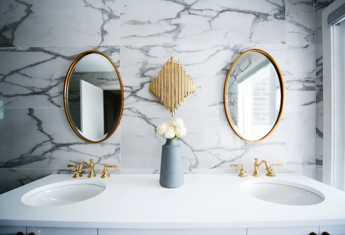 A marble-tiled bathroom with two round brass mirrors